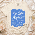 Cream t-shirt with "Her Last Rodeo" text, cowboy hat, and boots.