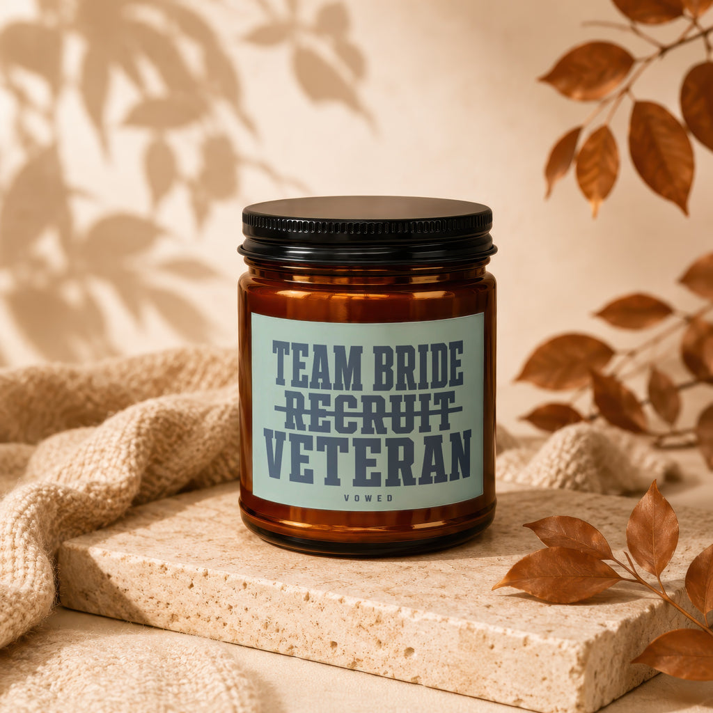Amber candle with black lid, label reads "Team Bride Recruit Veteran Vowed."