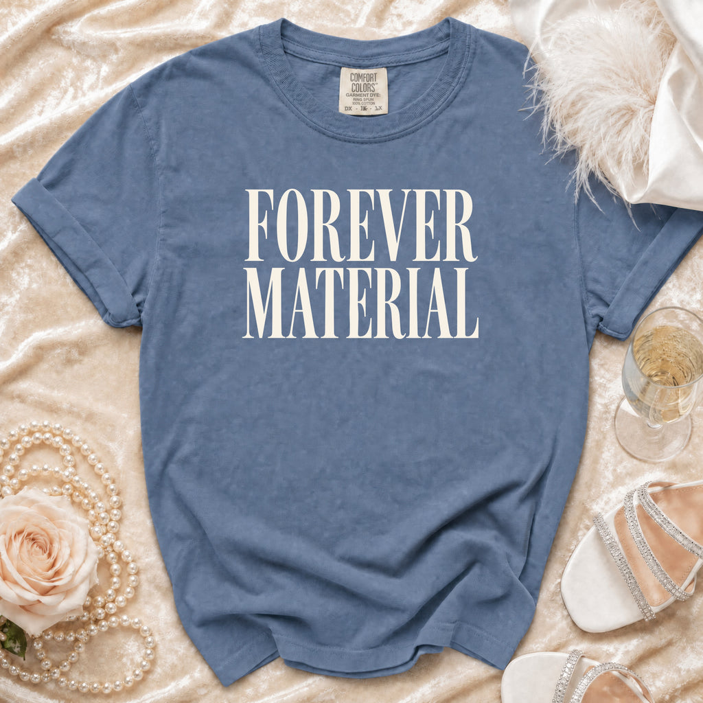 Blue t-shirt with "FOREVER MATERIAL" text, laid flat with decorative accessories.