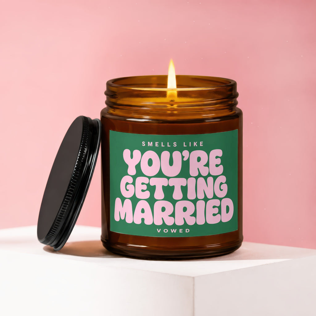 Amber candle with a lit wick on a white surface, label reads "Smells like You're Getting Married"