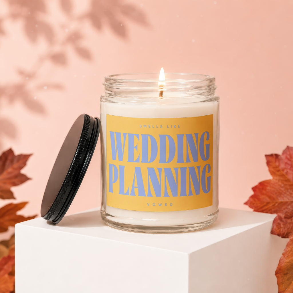 Candle with a lit wick and a yellow label reading "SMELLS LIKE WEDDING PLANNING VOWED".