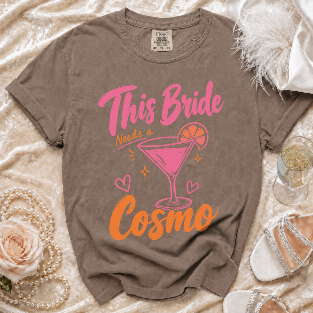 Taupe Comfort Colors t-shirt with pink and orange "This Bride Needs a Cosmo" graphic.