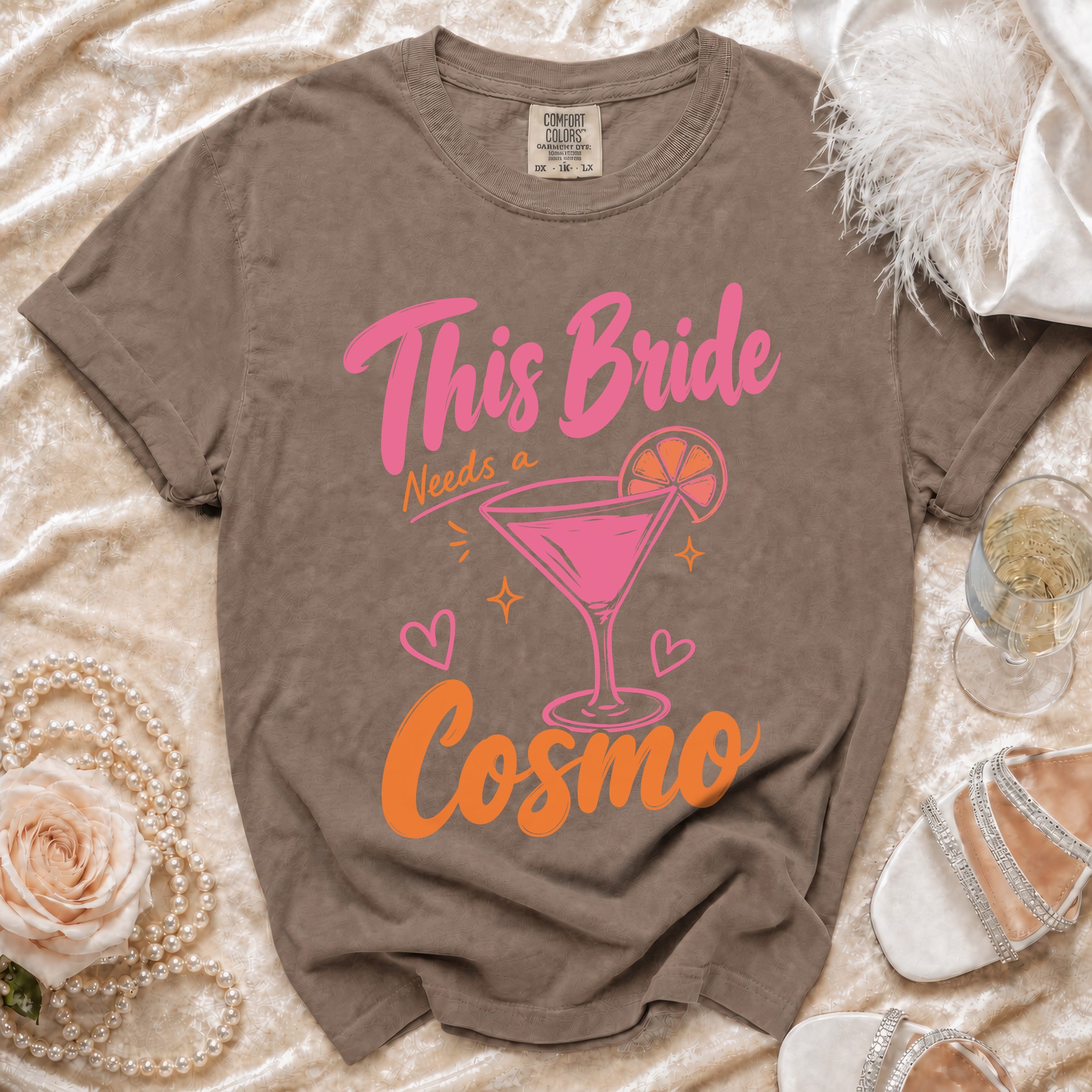 Taupe Comfort Colors t-shirt with pink and orange "This Bride Needs a Cosmo" graphic.