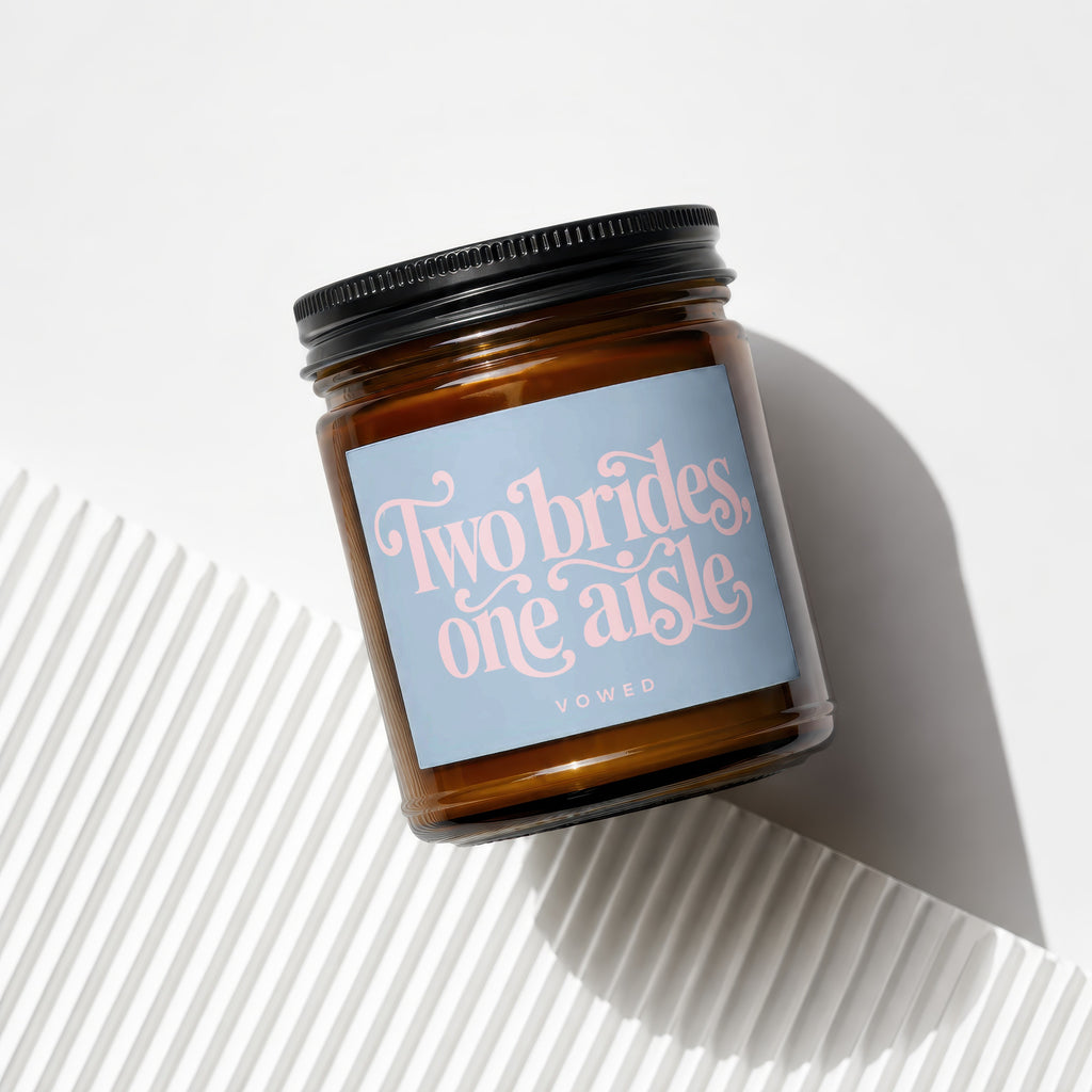Amber jar candle with a light blue label reading "Two brides, one aisle" and "VOWED".