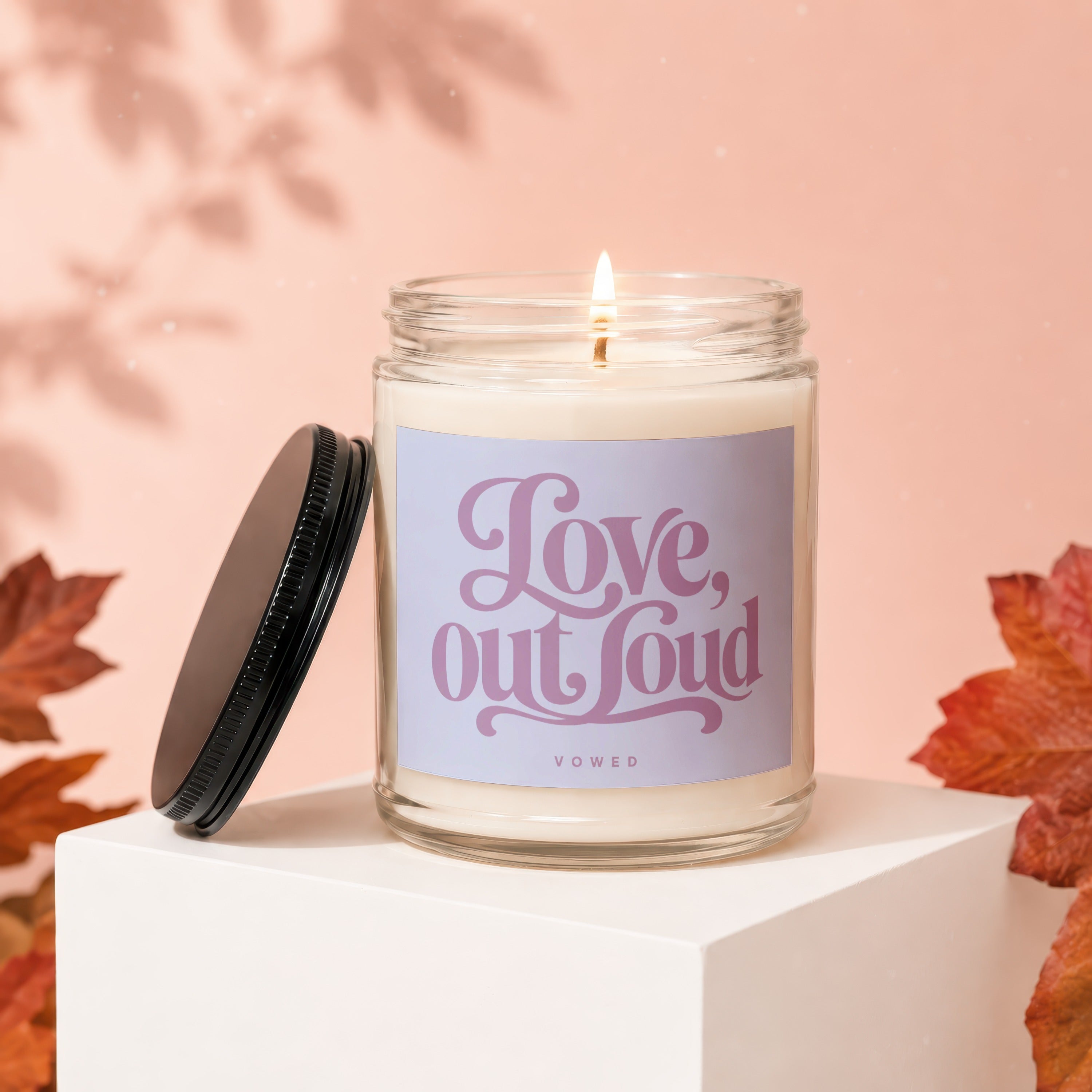 Lit candle with "Love, out loud" text on a jar with lid beside it.