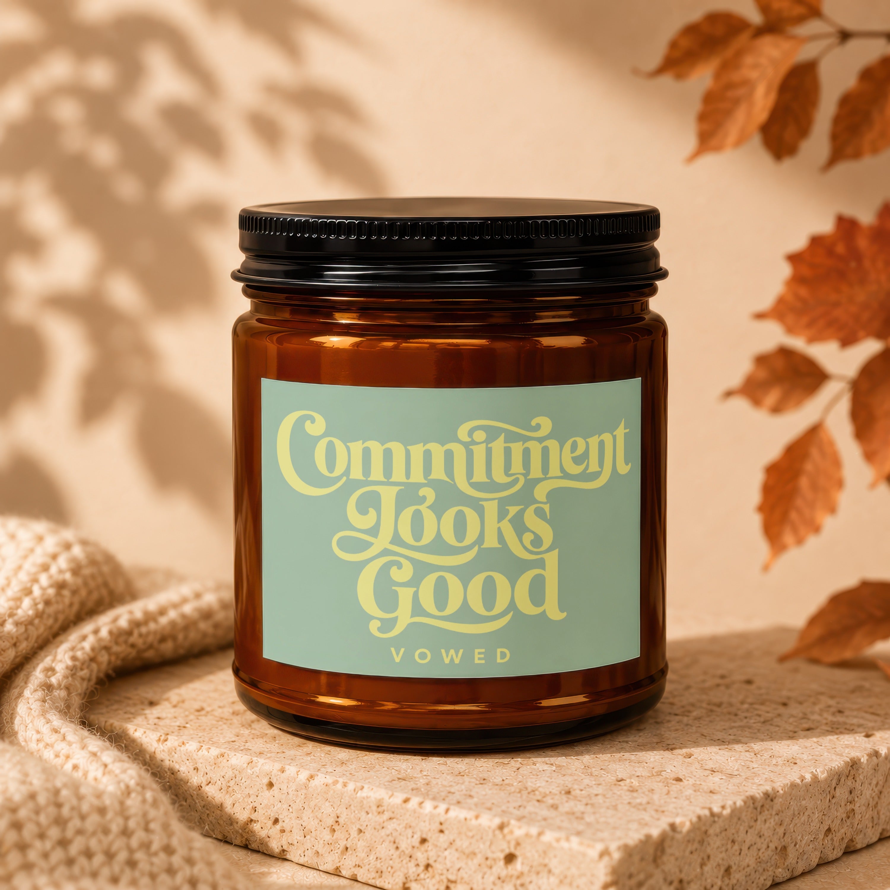 Amber glass candle with "Commitment Looks Good" and "vowed" text on a light green label.