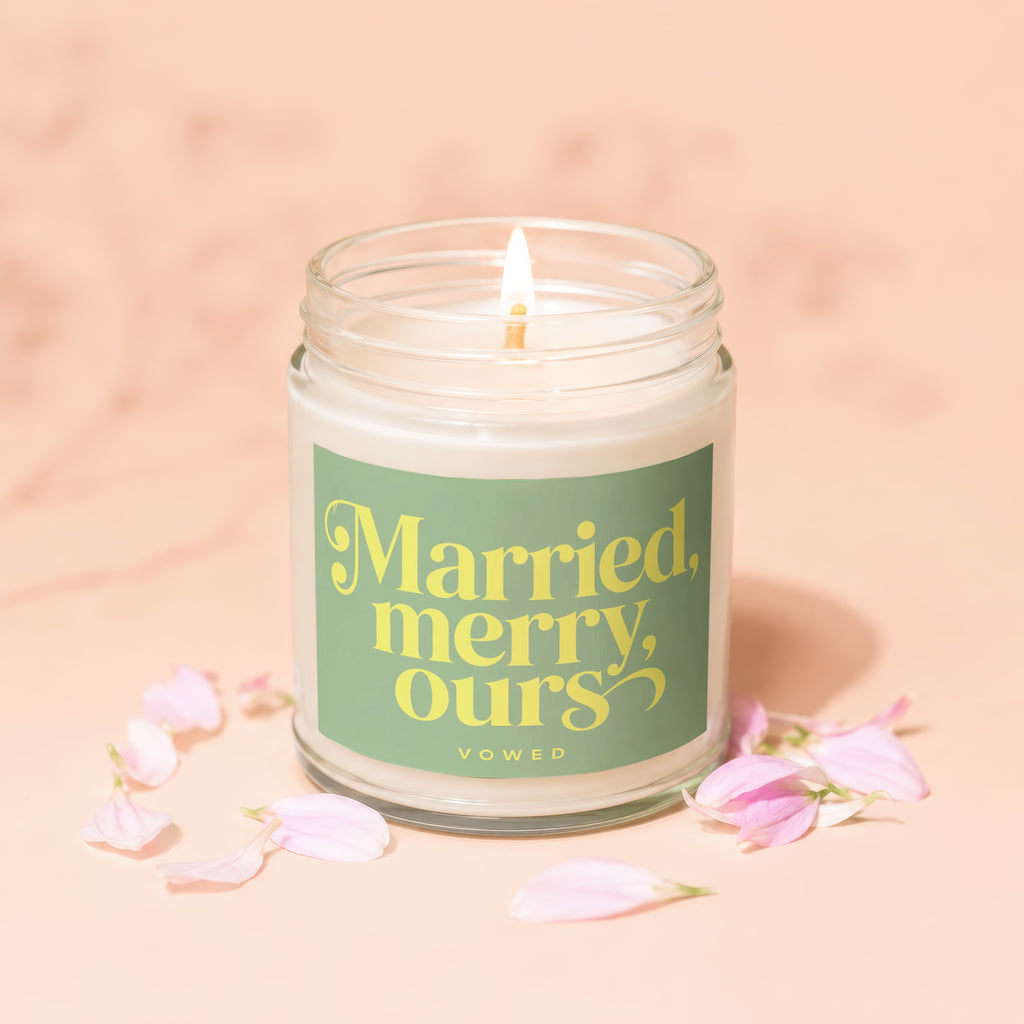 Lit candle in glass jar with "Married, merry, ours" text and petals.