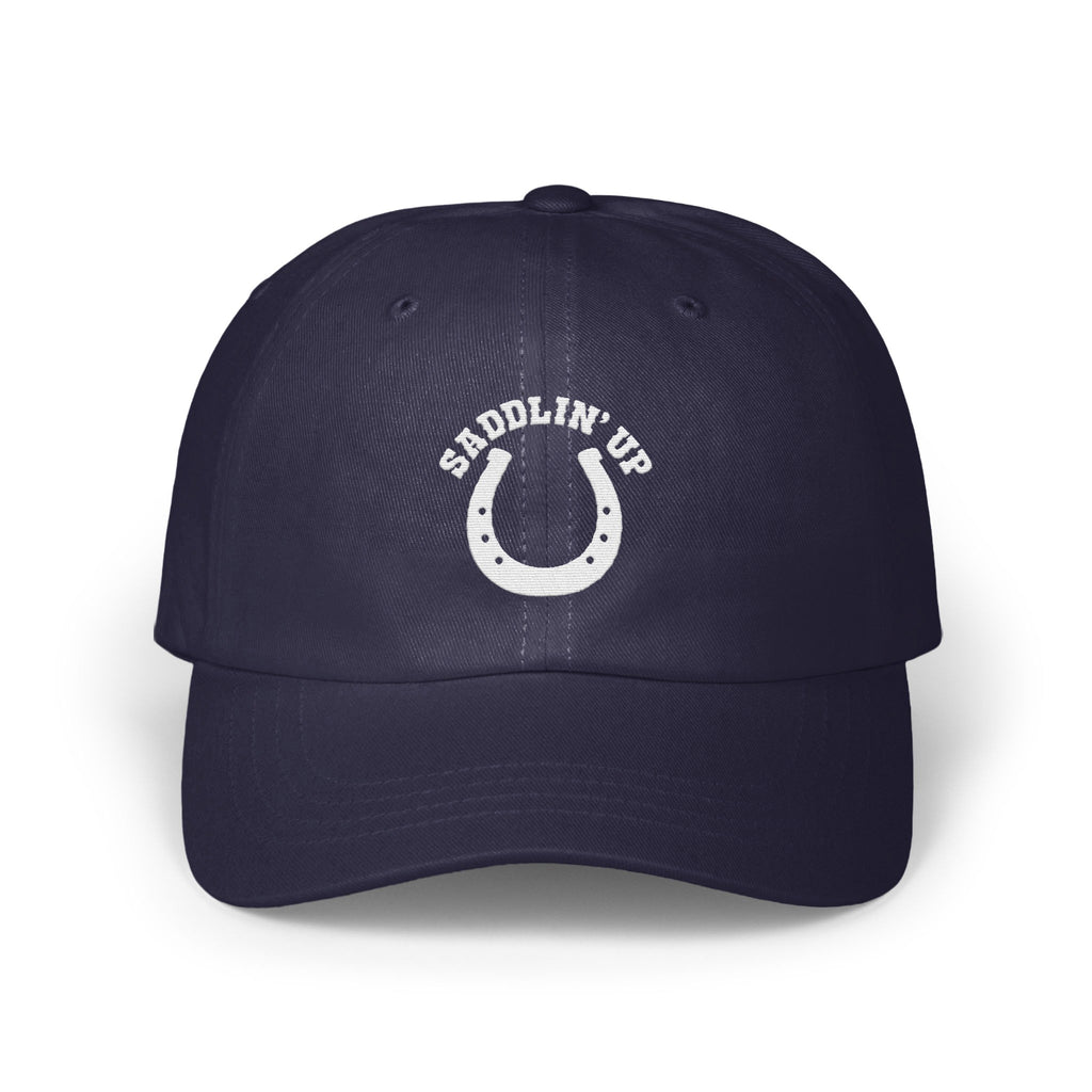 A dark blue baseball cap with white embroidery featuring a horseshoe and the text SADDLIN' UP.