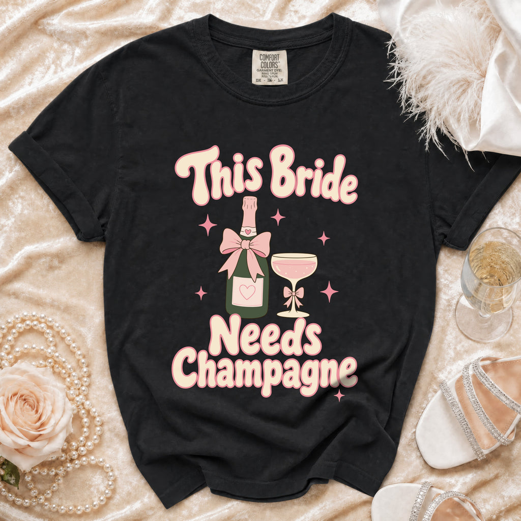 Black t-shirt with "This Bride Needs Champagne" text, bottle, and Champagne glass graphic.