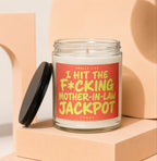 Glass candle with bright orange label stating "SMELLS LIKE I HIT THE F*CKING MOTHER-IN-LAW JACKPOT VOWED."