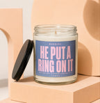 Glass candle with blue label that reads "WARNING: HE PUT A RING ON IT" and smaller text.