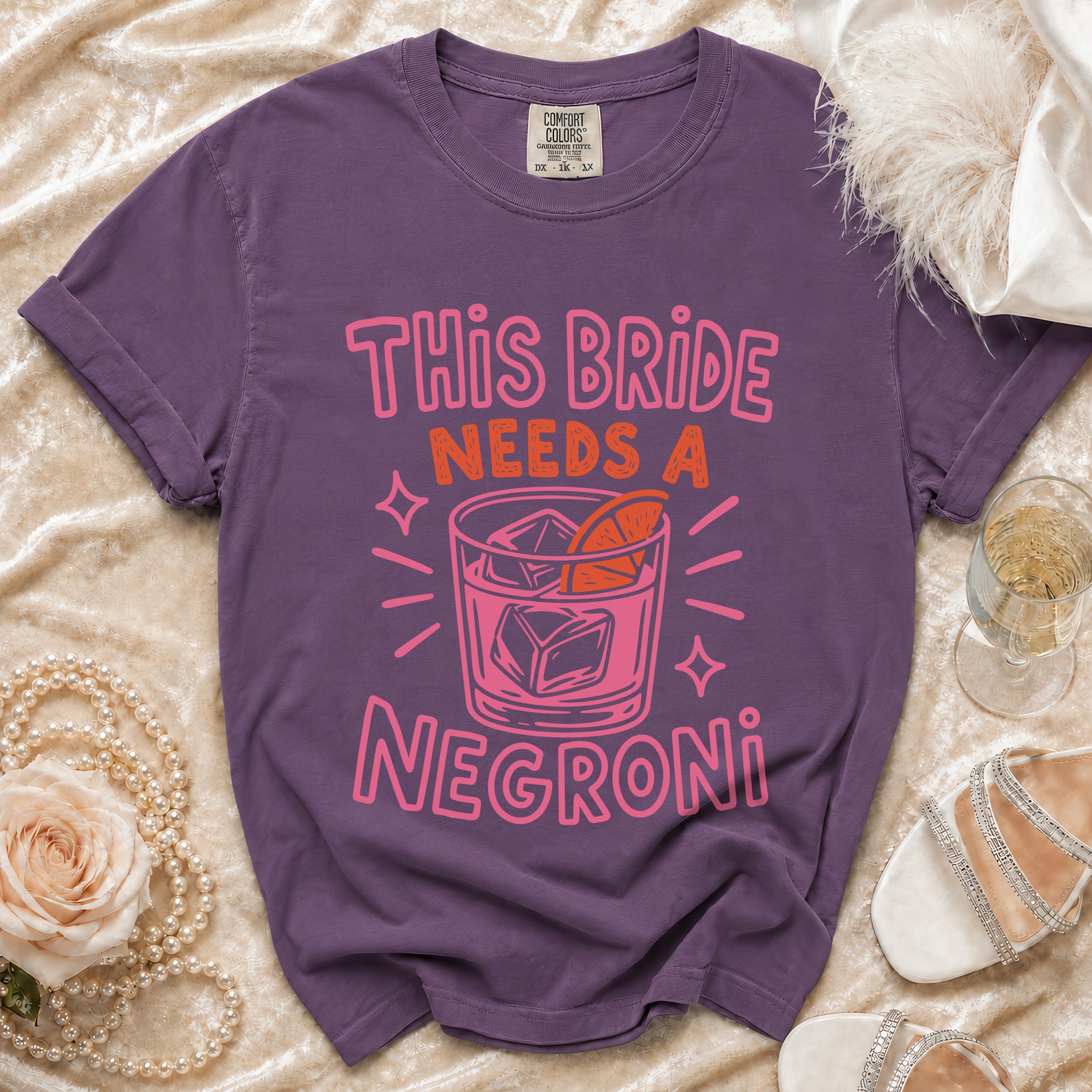 Purple t-shirt with pink text "This Bride Needs a Negroni" and a cocktail illustration.