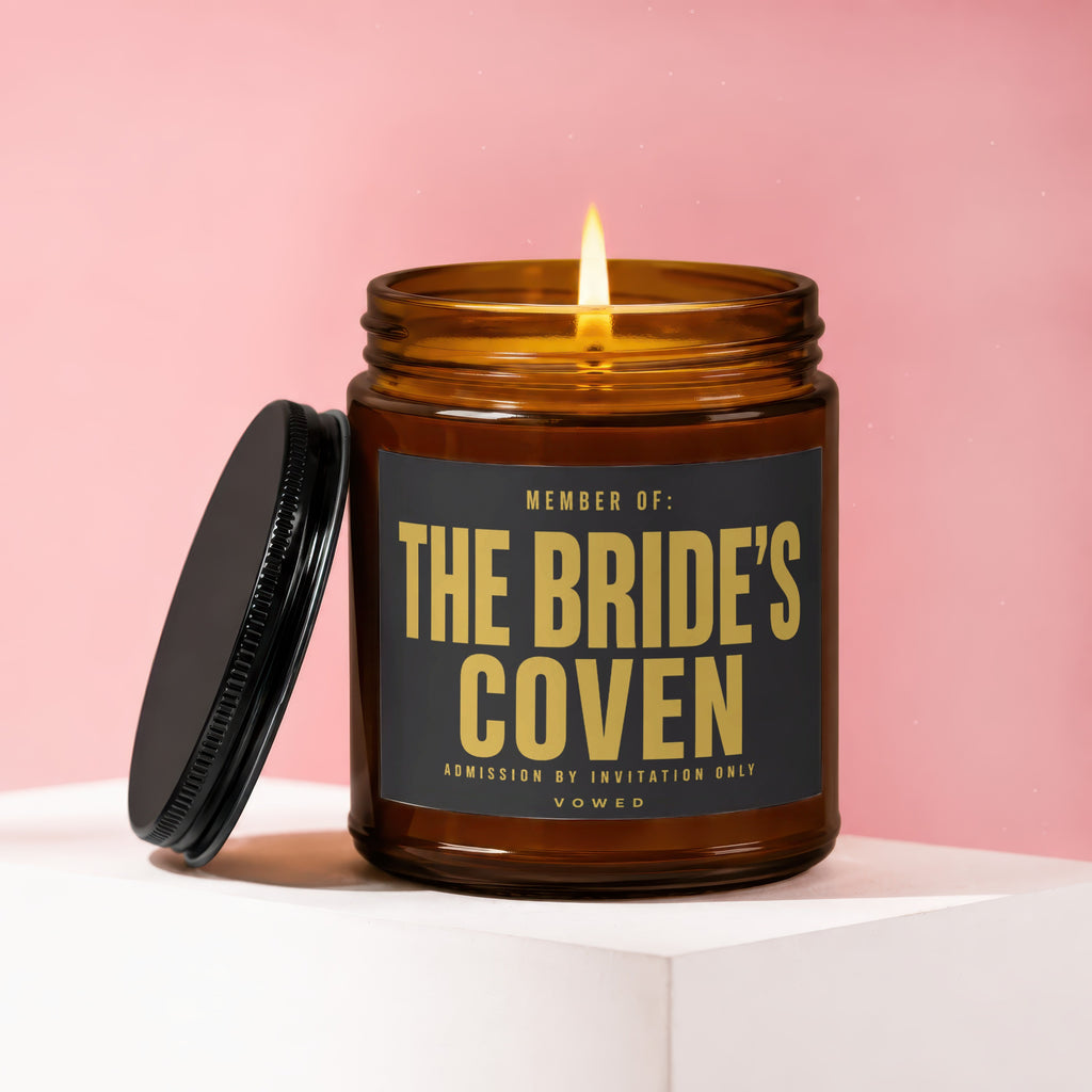 Amber glass candle with black lid displays "THE BRIDE'S COVEN ADMISSION BY INVITATION ONLY..." text.