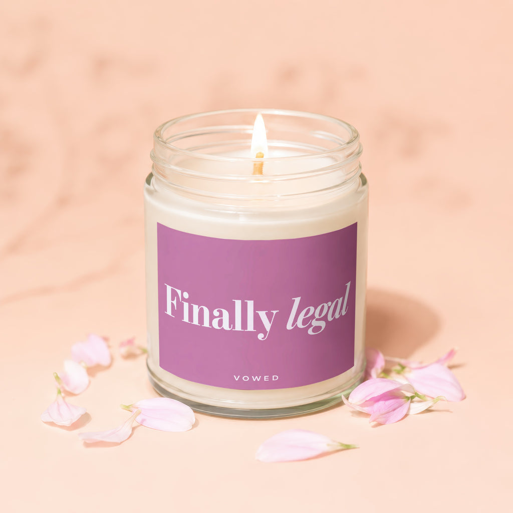 Glass jar candle with lit flame, purple label says "Finally legal VOWED."