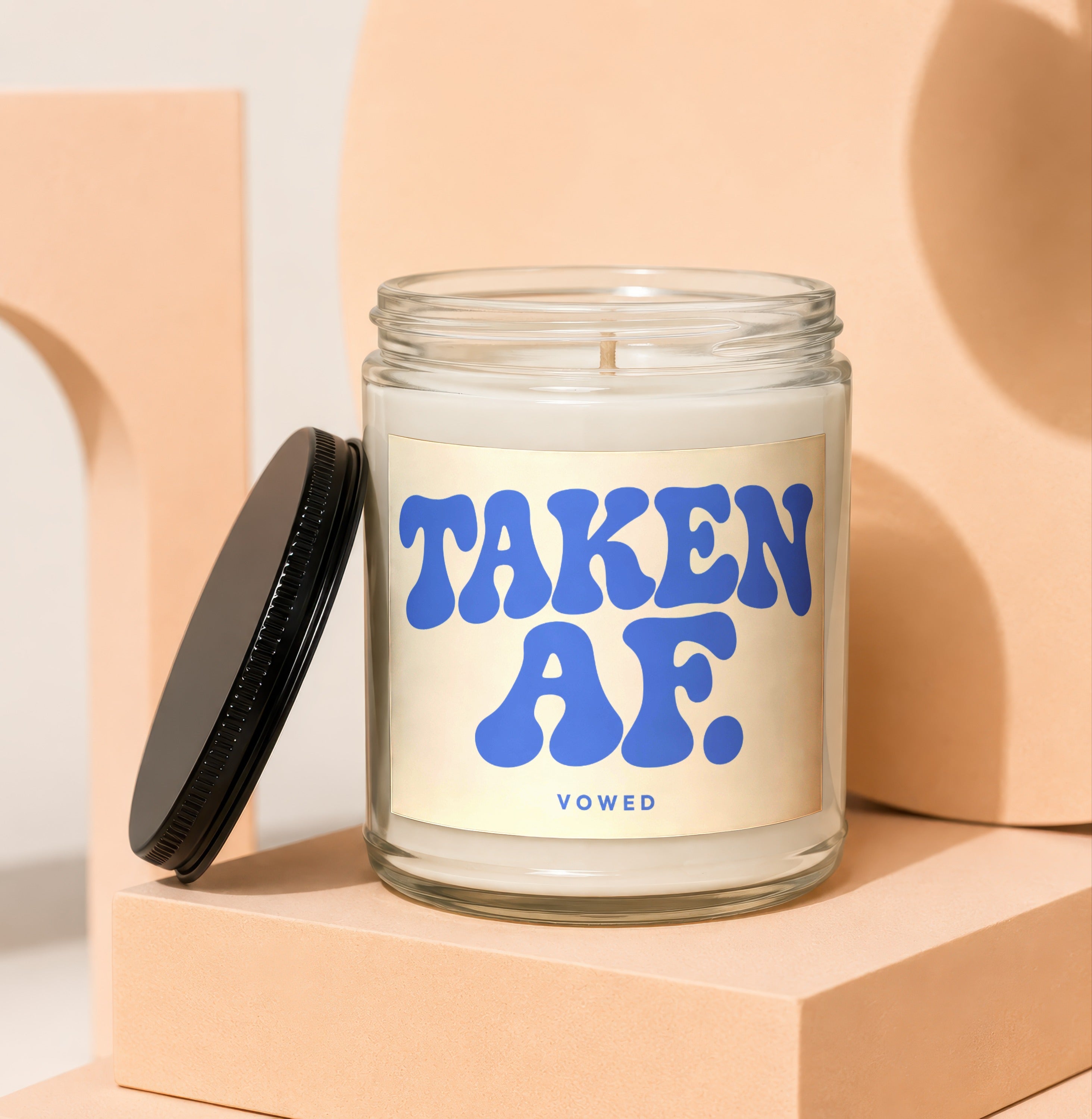 Glass candle with "TAKEN AF. VOWED" text on a light beige label and a black lid.