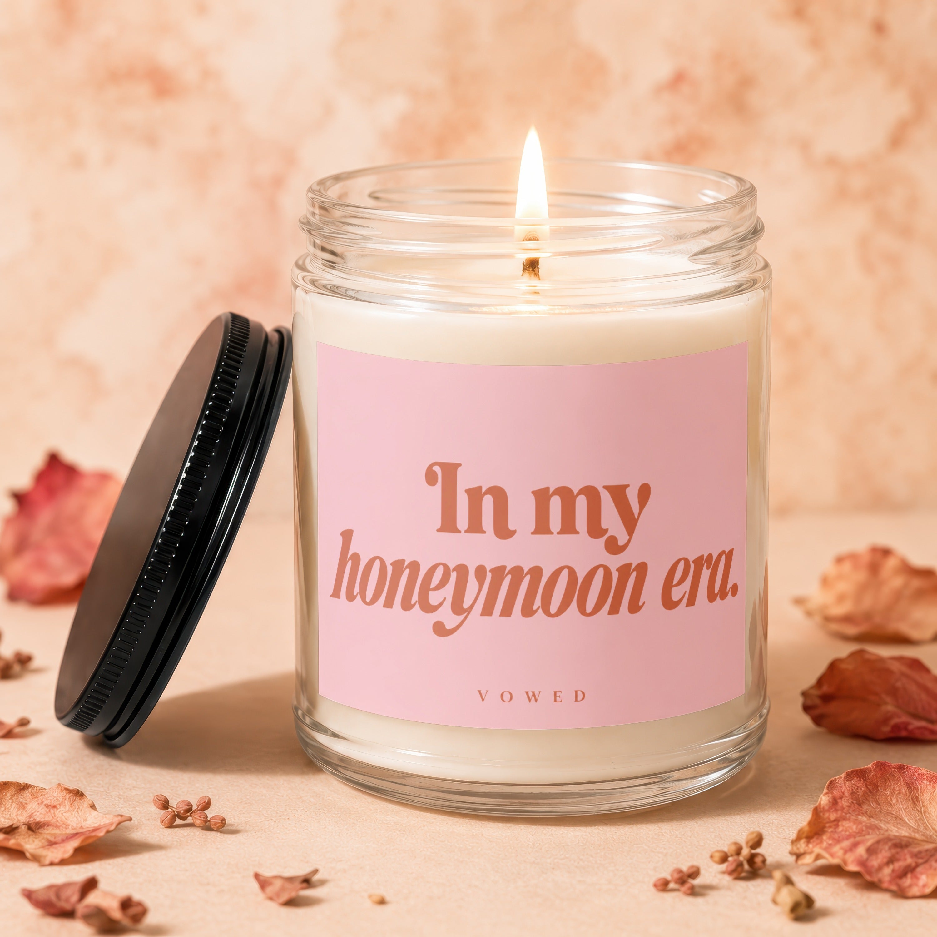 Candle with pink label reading "In my honeymoon era. VOWED" on peach background.