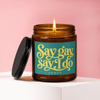 Amber jar candle with lit wick and black lid. Text says "Say gay say I do" with "vowed".