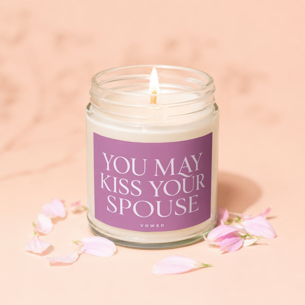 Lit candle in glass jar with "You May Kiss Your Spouse" text and petals.