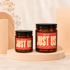 Two amber glass candles with "JUST US" on red labels.