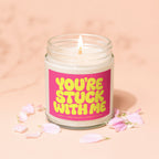 Jar candle with lit wick and pink label reading "YOU'RE STUCK WITH ME".