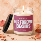 Candle with text "Our Forever Begins" and "Vowed" on burgundy label.