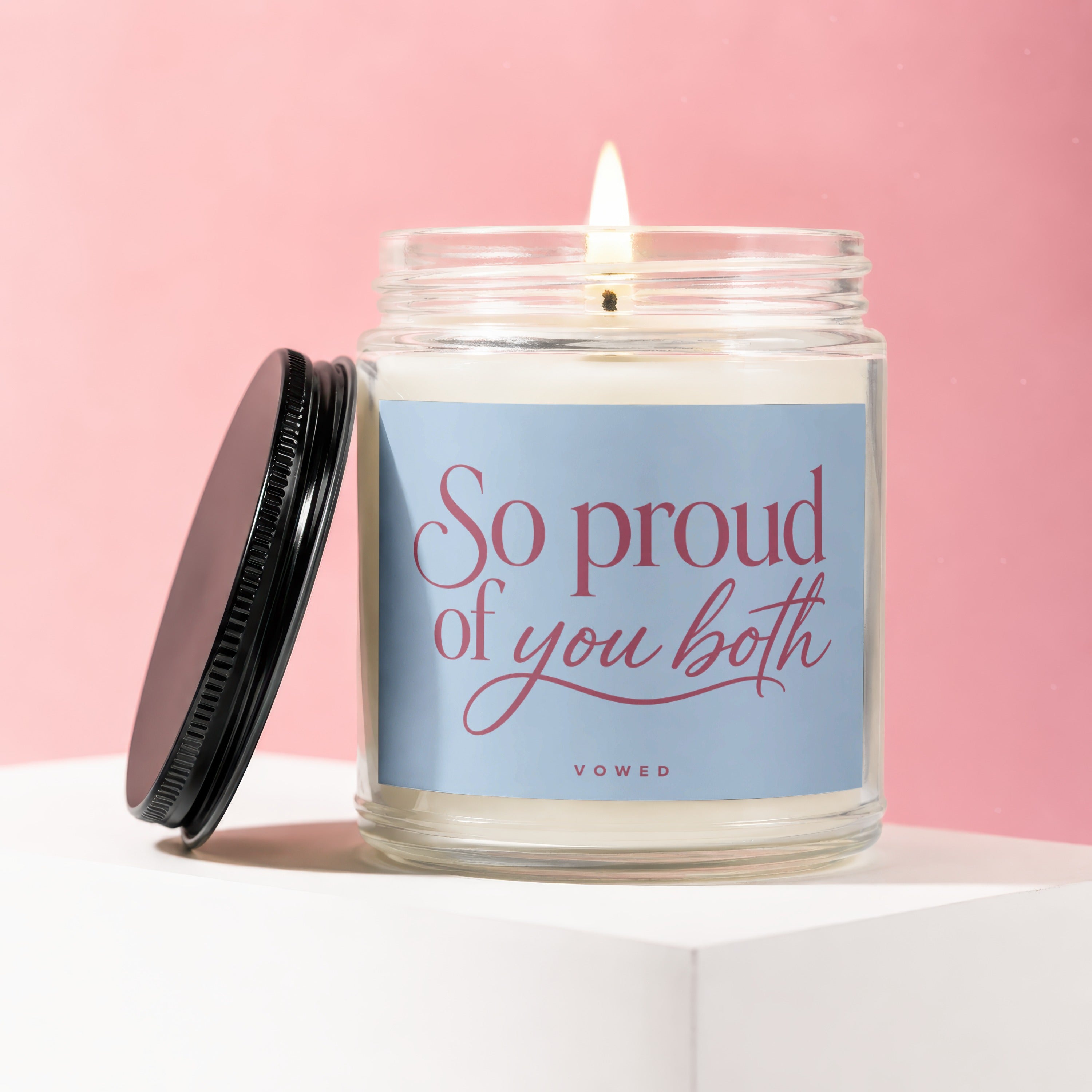 Candle with pink text "So proud of you both" on a blue label.