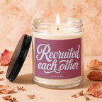 Jar candle with lit flame and burgundy label reading "Recruited each other"