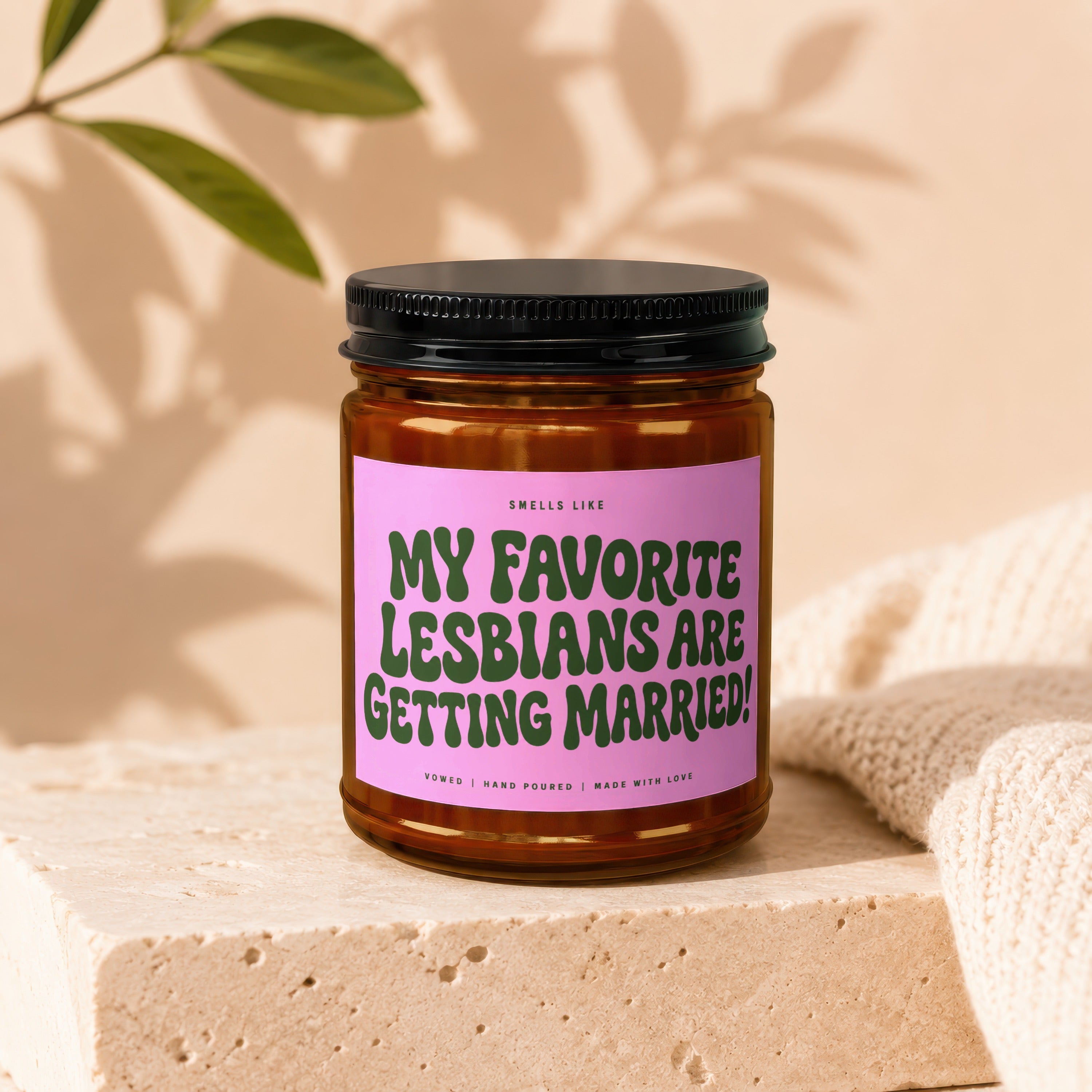 Amber jar candle with pink label reading "MY FAVORITE LESBIANS ARE GETTING MARRIED!"