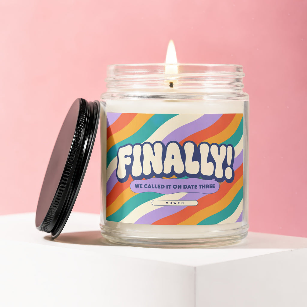 Glass jar candle with colorful wavy stripe label reading "FINALLY! WE CALLED IT ON DATE THREE VOWED".