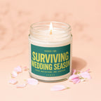 Glass candle jar with lit wick reading "Surviving Wedding Season".