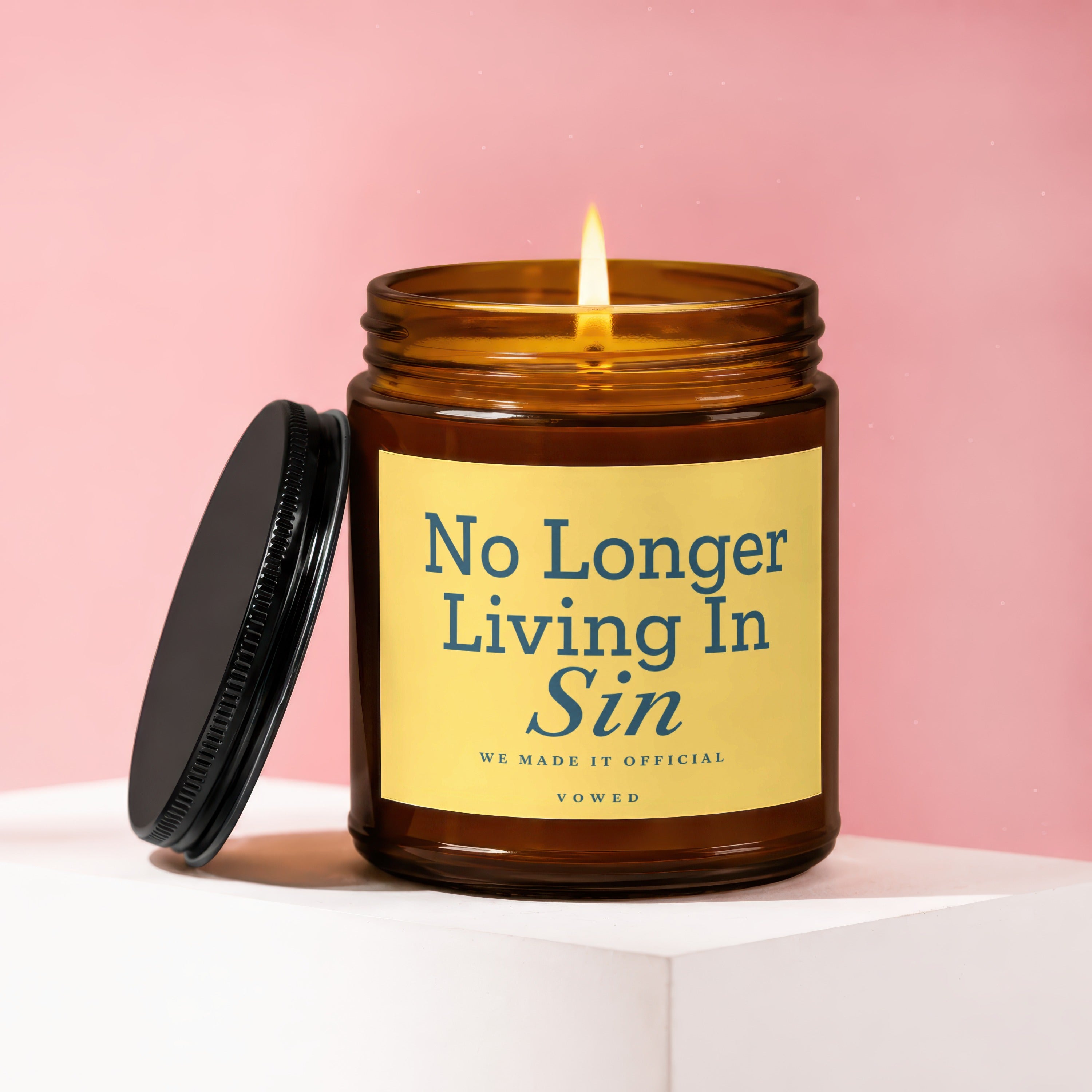 Amber glass candle with a lit wick and lid, reading "No Longer Living In Sin."