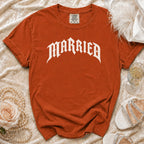 Orange t-shirt with white "MARRIED" text, laid flat with decorative items.