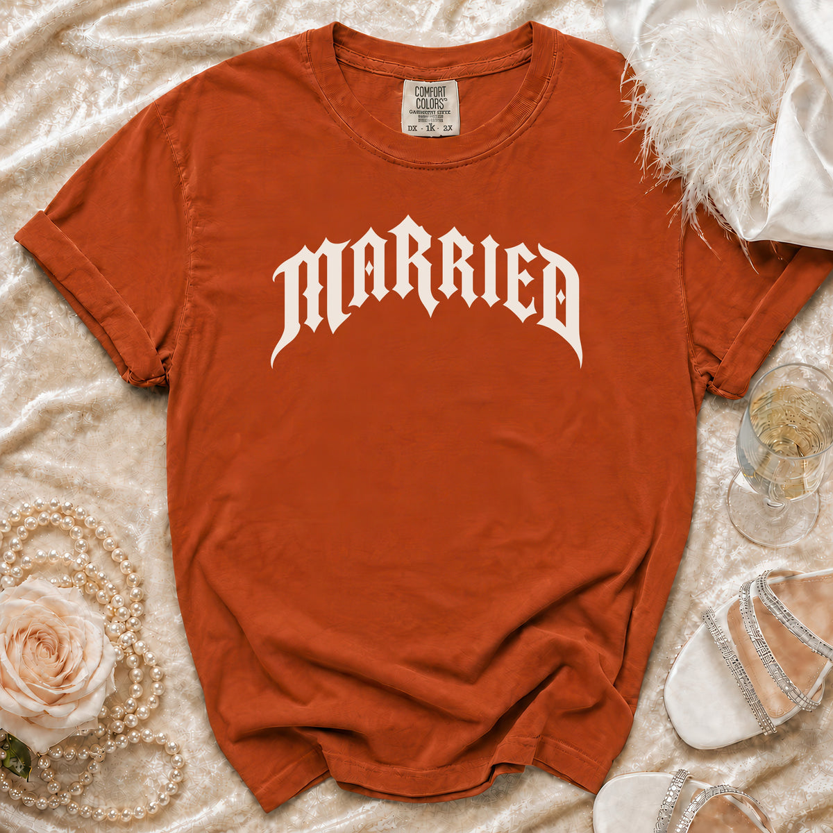 Orange t-shirt with white "MARRIED" text, laid flat with decorative items.