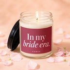 Glass candle with lit wick on peach background, surrounded by pink petals. Text reads "In my bride era. VOWED".