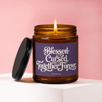 Amber jar candle with lit flame, lid to the side, and "Blessed Cursed Together Forever VOWED" text.