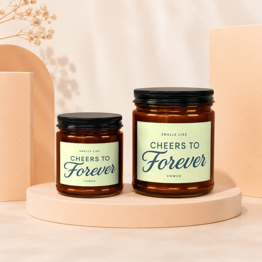 Two glass candles with black lids, labeled "Cheers to Forever".