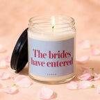 Candle with black lid off, lit wick, reads "The brides have entered VOWED".
