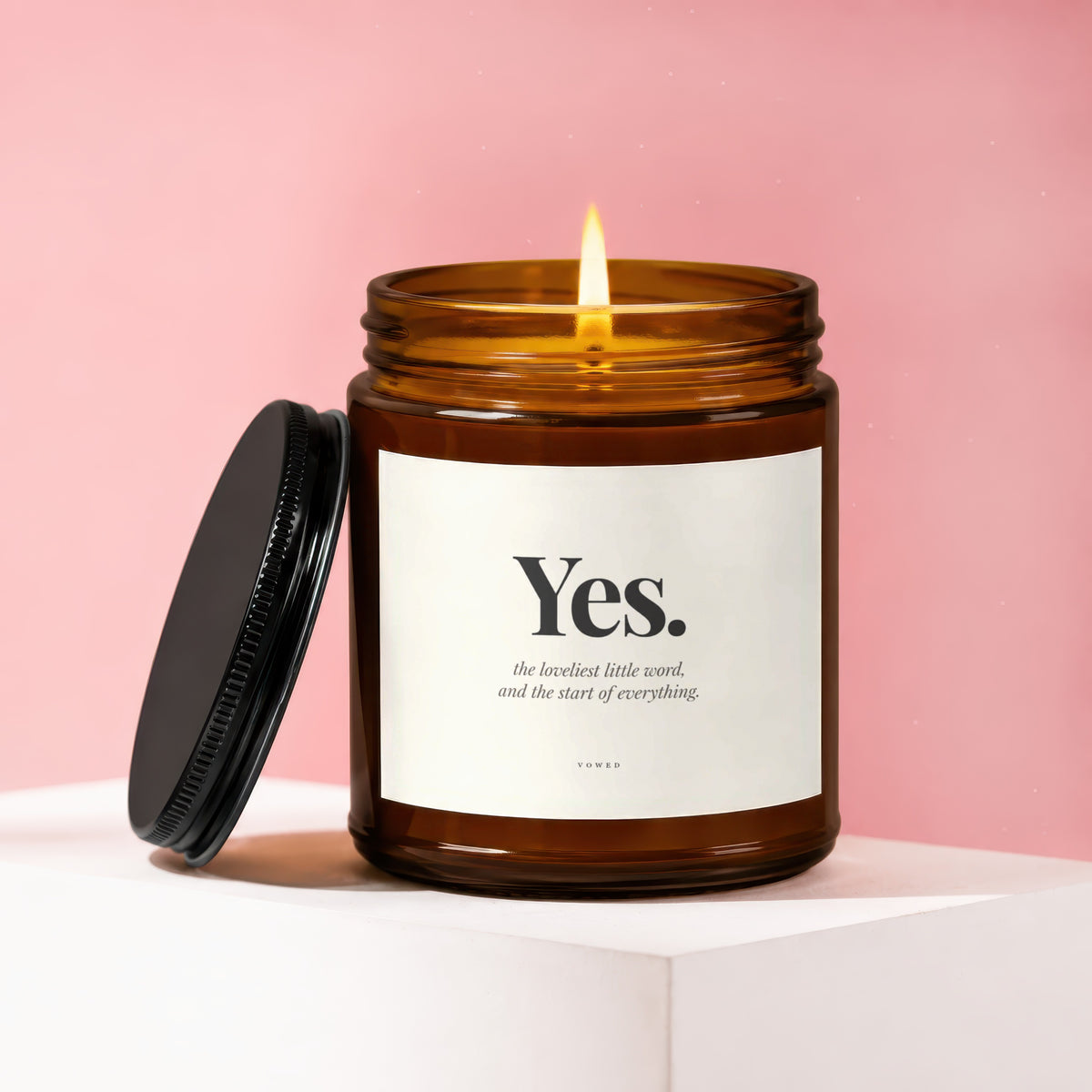 Amber candle with black lid, lit flame, and "Yes." text.