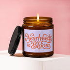 Amber glass candle with lit wick and label reading "Nearlyweds in Bloom VOWED".