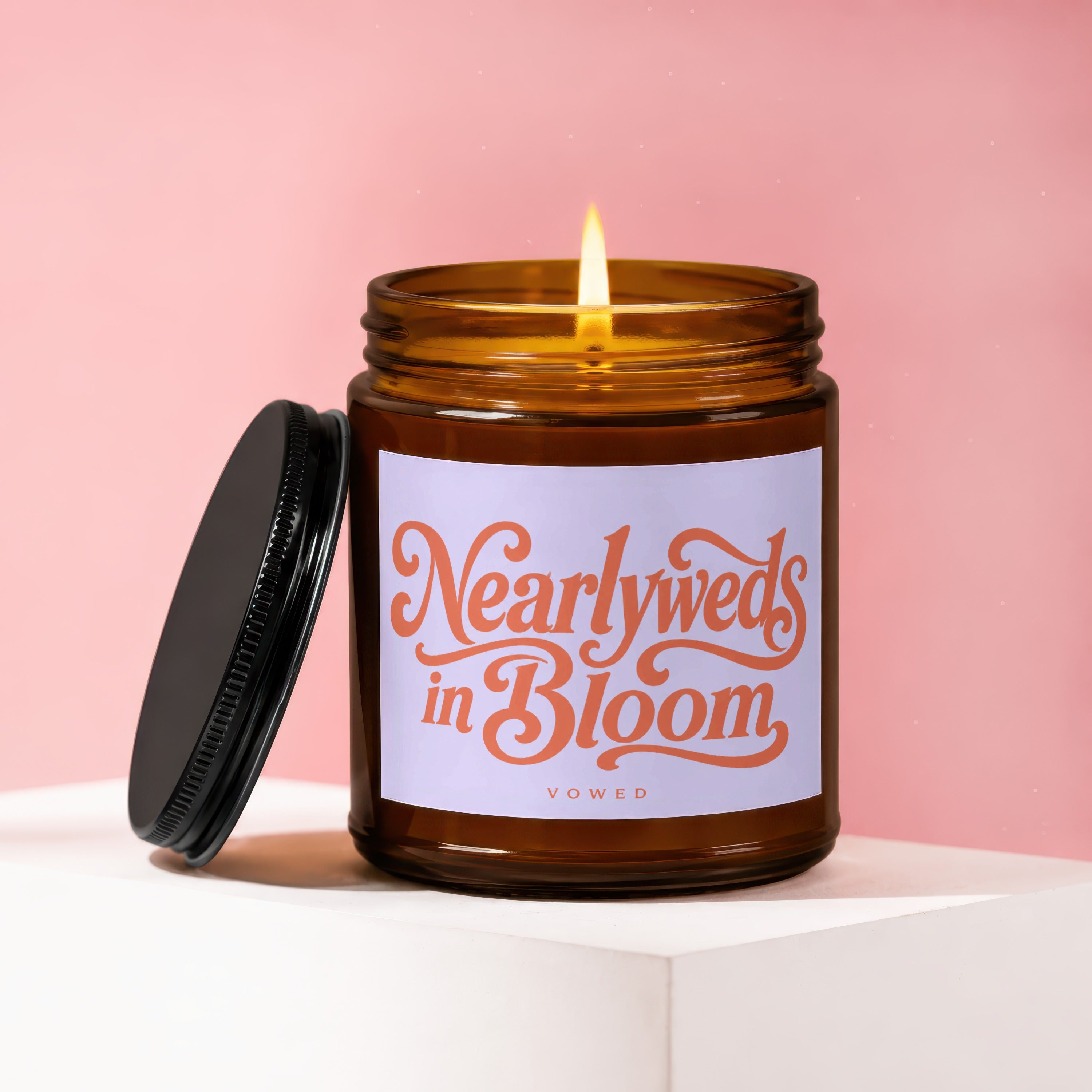 Amber glass candle with lit wick and label reading "Nearlyweds in Bloom VOWED".