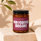 Glass jar candle with "Our Forever Begins" label, celebrating a vow.