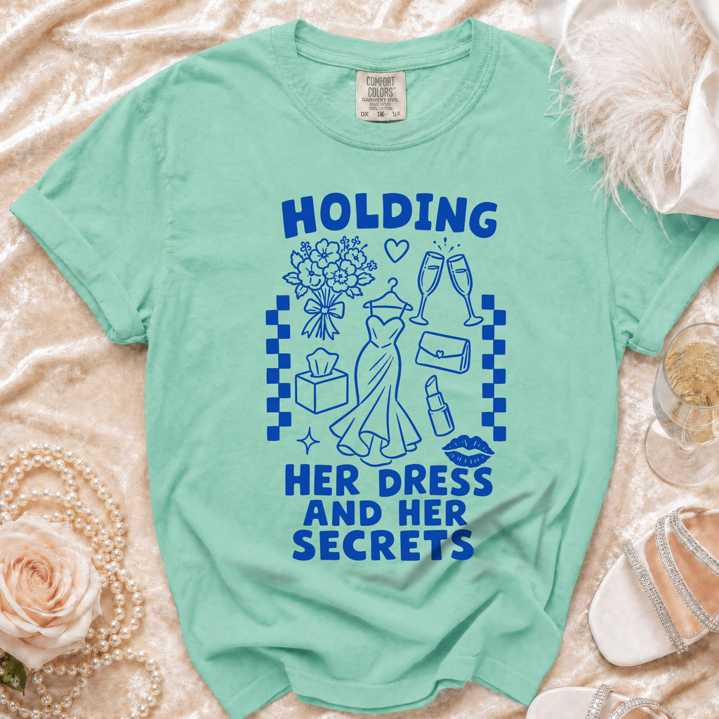 Teal t-shirt with blue graphic text "HOLDING HER DRESS AND HER SECRETS".
