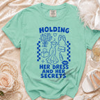 Teal t-shirt with blue graphic text "HOLDING HER DRESS AND HER SECRETS".
