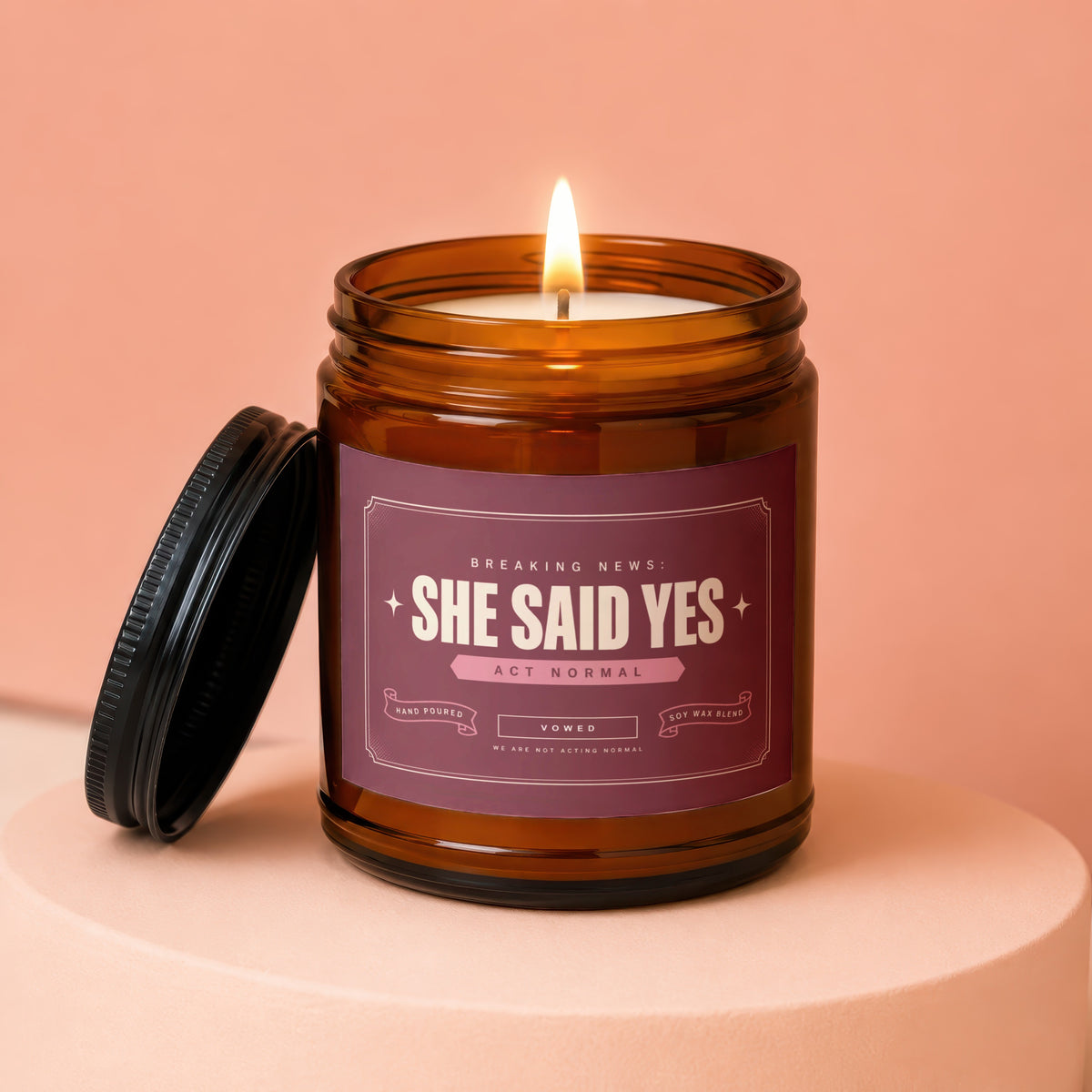 Amber glass candle labeled "She Said Yes" with a lit wick and black lid.