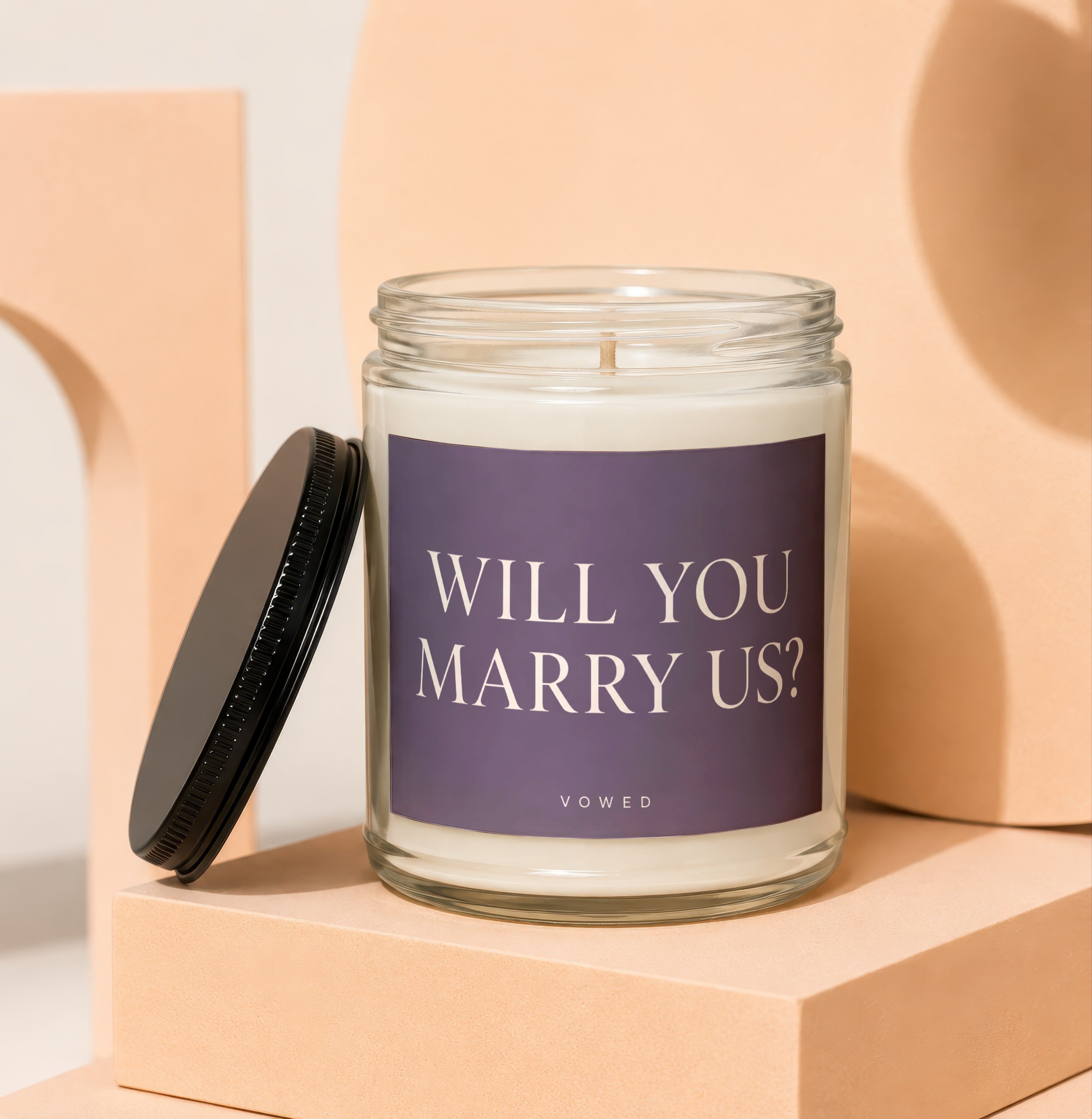 Glass candle with purple label that reads "WILL YOU MARRY US? VOWED".