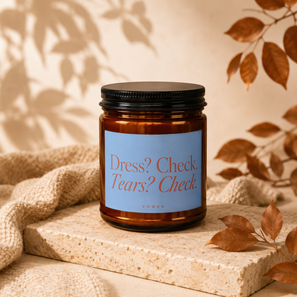 Brown glass candle with blue label reading "Dress? Check. Tears? Check. VOWED."