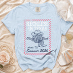 Light blue t-shirt with "Reckless in Texas Olivia Bach Austin, Summer 2026" text and graphics.