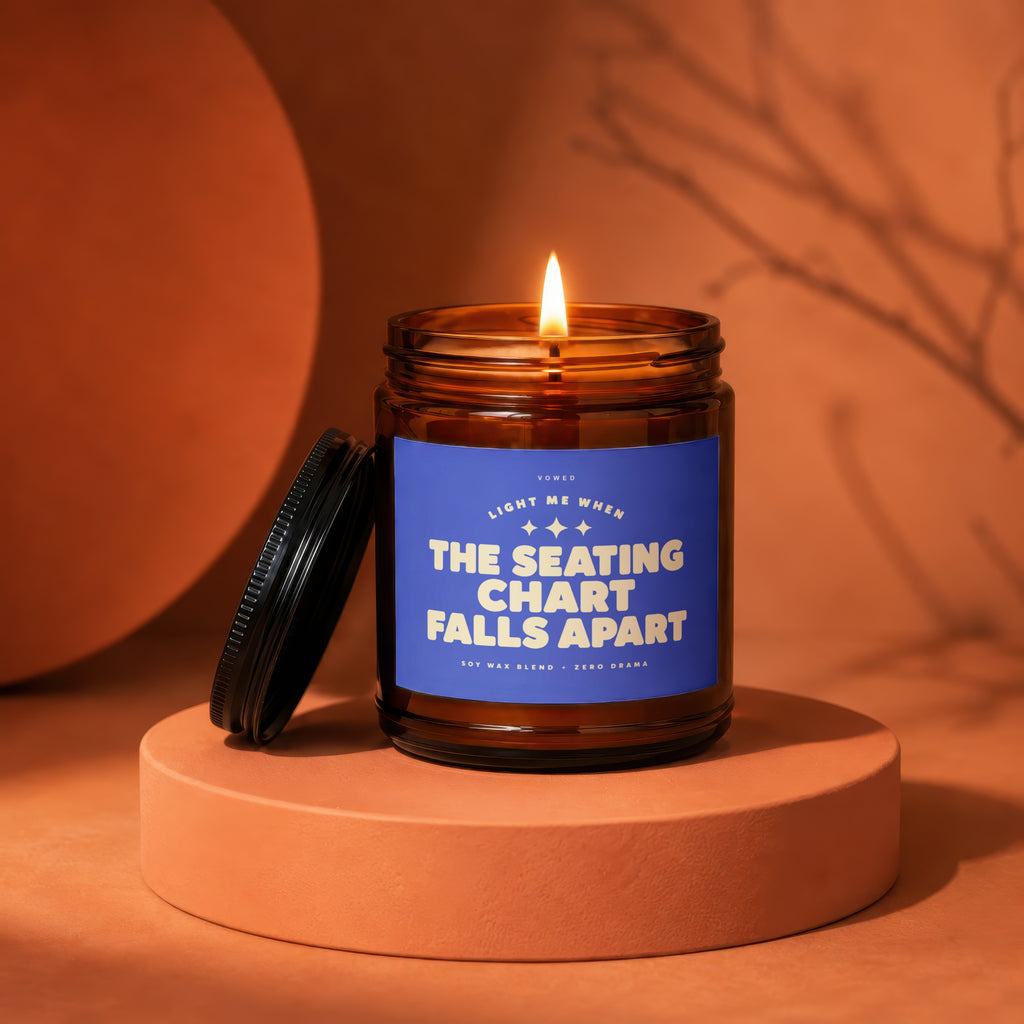 Amber candle with lit flame, reads "The Seating Chart Falls Apart".
