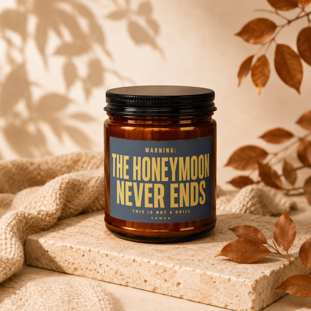 Amber jar candle with dark blue label reading "WARNING: THE HONEYMOON NEVER ENDS".