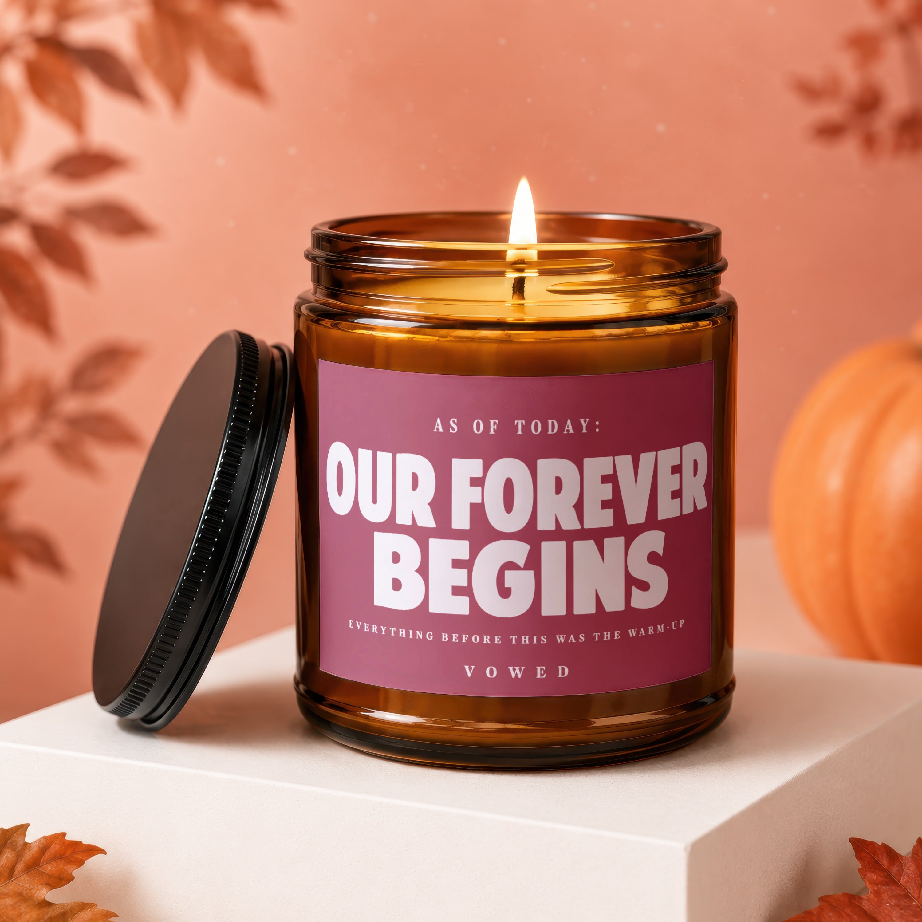 Brown glass candle with "Our Forever Begins" text, lit wick, and pumpkin.